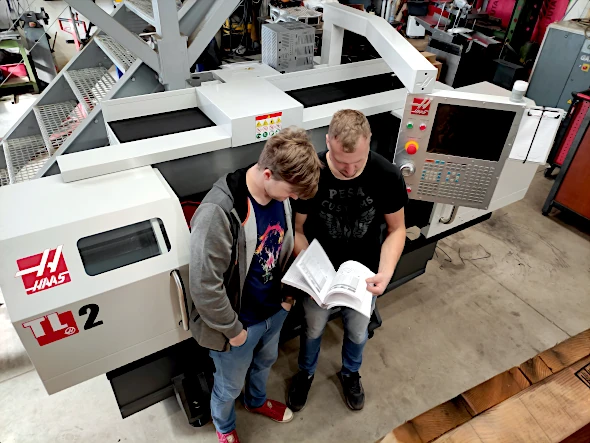 AMI engineers discussing project plans beside a CNC lathe machine in Latvia.